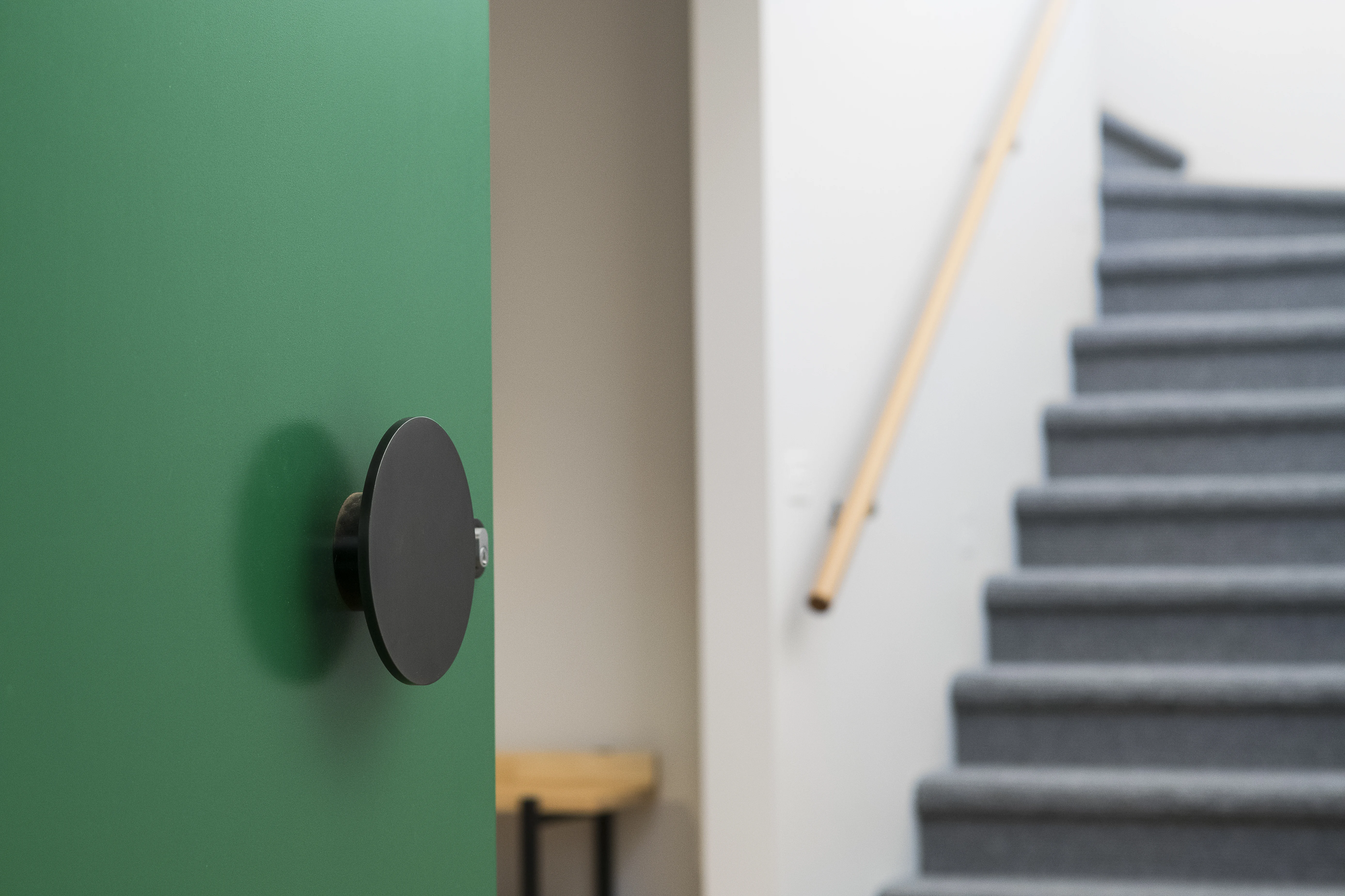 Green door with round handle next to carpeted stairs.