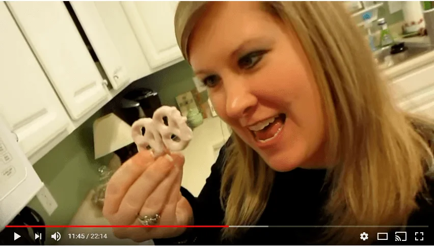 Woman holding yogurt-covered pretzels in a kitchen.