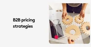 Two people holding wooden gears over a laptop, symbolizing B2B pricing strategies.