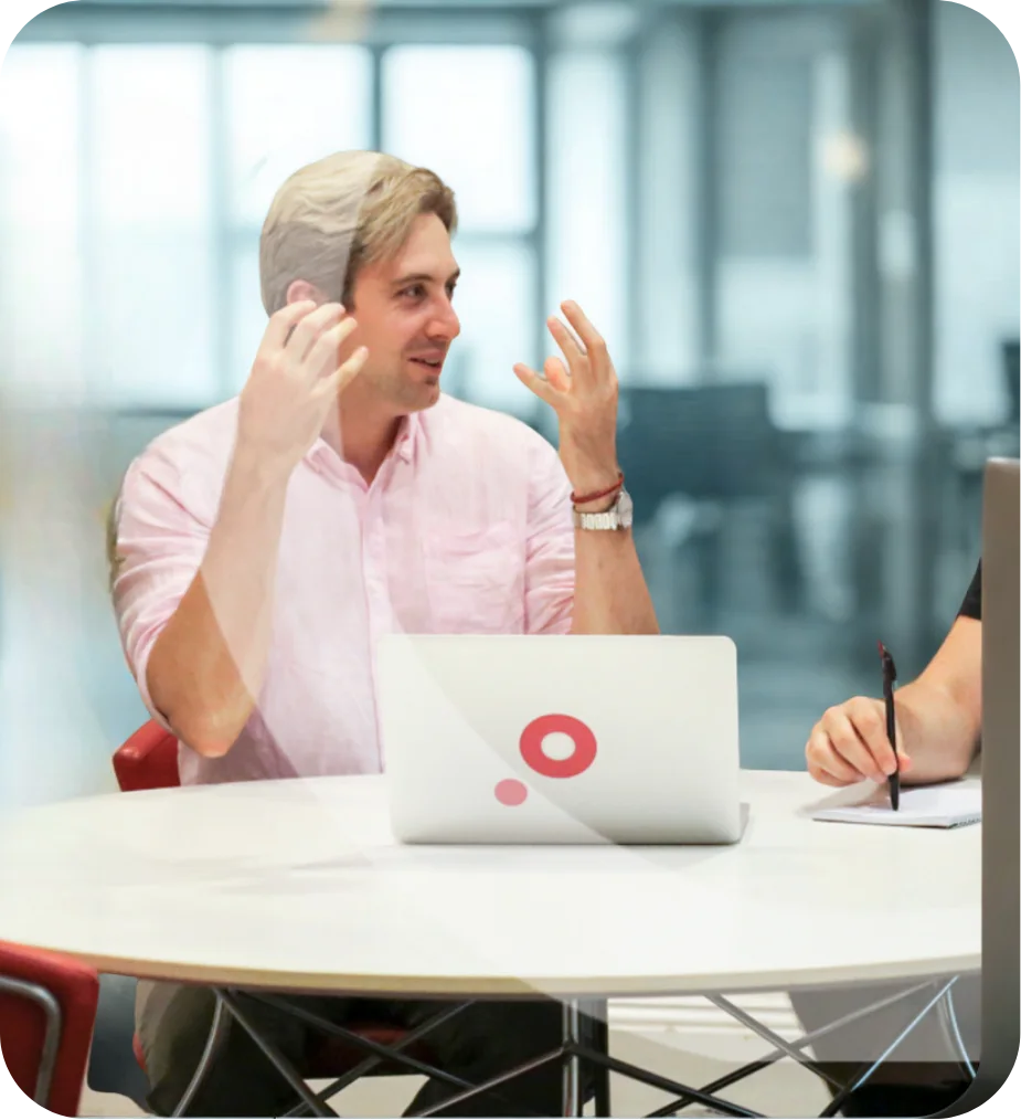 Two people discussing at a round table with a laptop in an office setting.