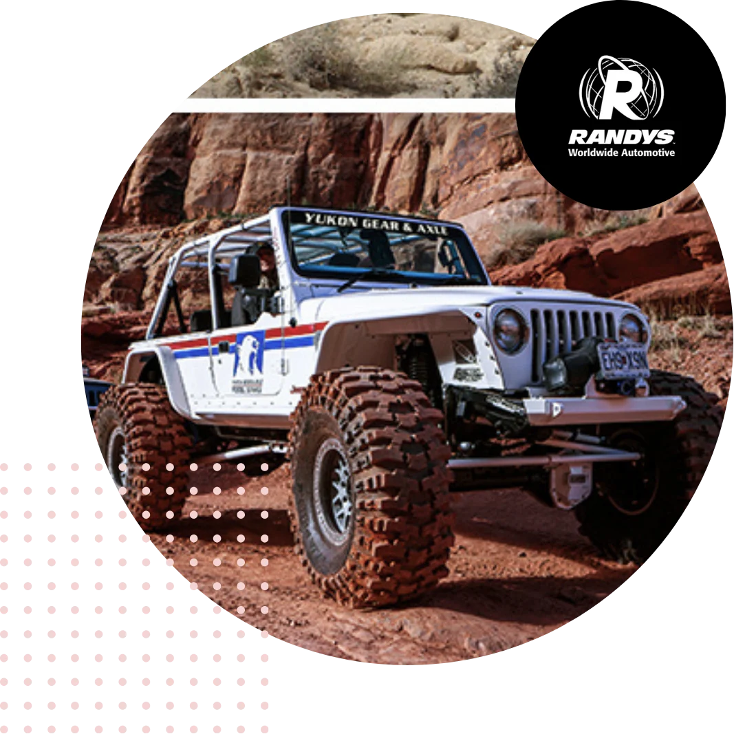 White jeep with large tires off-roading on rocky terrain with Randys logo.