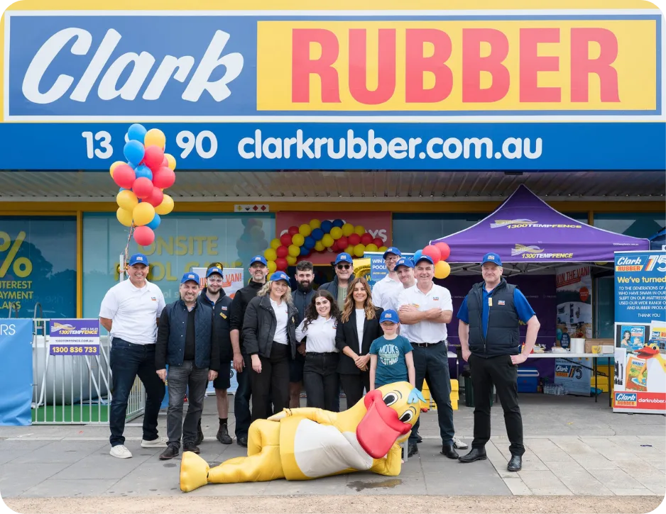 Group of people at Clark Rubber store opening event with balloons and signage.